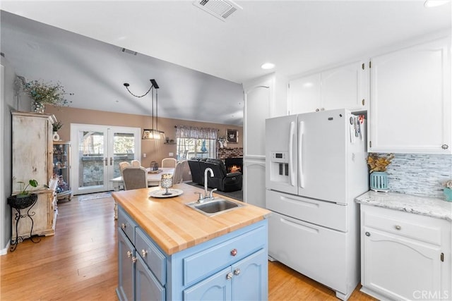 kitchen featuring a center island with sink, white cabinets, french doors, blue cabinets, and white fridge with ice dispenser