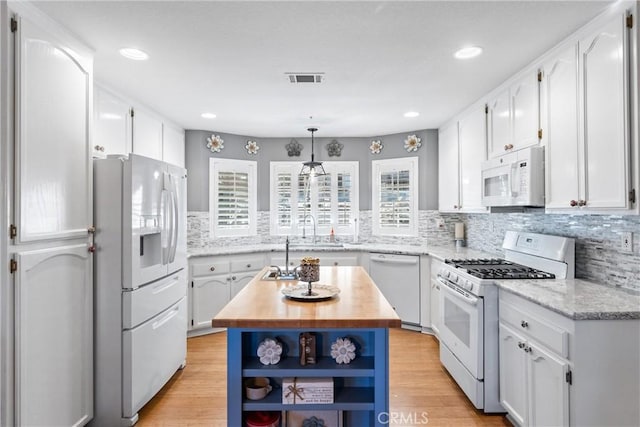 kitchen featuring white cabinets, a center island, butcher block countertops, and white appliances