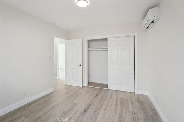 unfurnished bedroom featuring a wall mounted AC, a closet, and light hardwood / wood-style flooring