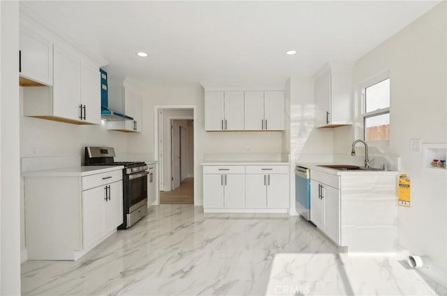 kitchen featuring wall chimney range hood, white cabinets, appliances with stainless steel finishes, and sink