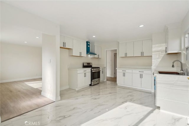 kitchen with stainless steel range, wall chimney exhaust hood, white cabinets, and sink