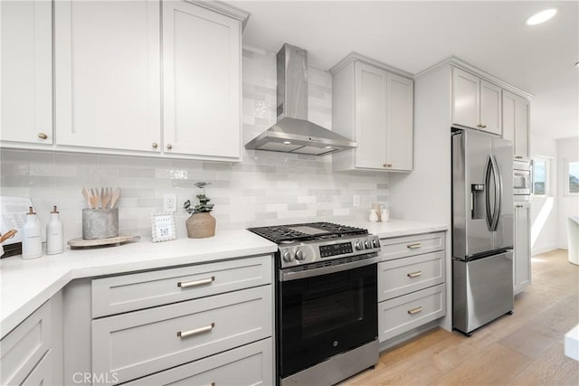 kitchen with tasteful backsplash, stainless steel appliances, wall chimney exhaust hood, and light wood-type flooring