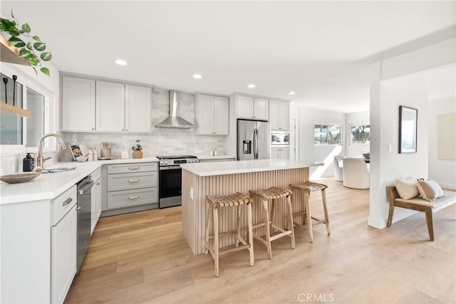 kitchen with appliances with stainless steel finishes, a center island, wall chimney exhaust hood, sink, and a breakfast bar area