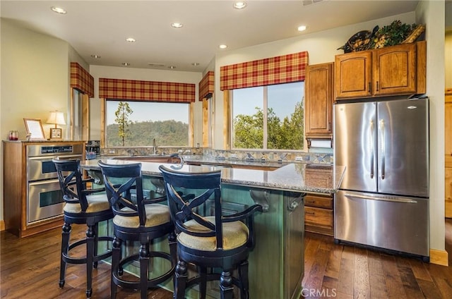 kitchen featuring a breakfast bar area, stainless steel appliances, dark wood-type flooring, light stone countertops, and a center island