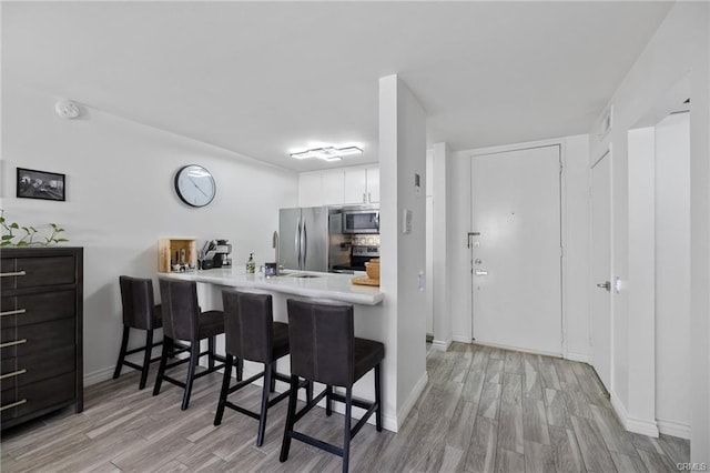 kitchen featuring a breakfast bar, kitchen peninsula, white cabinetry, light wood-type flooring, and stainless steel appliances