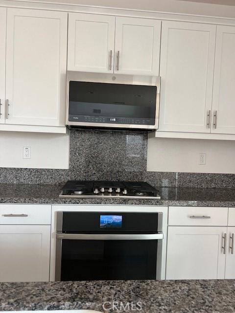 kitchen with white cabinetry, appliances with stainless steel finishes, dark stone counters, and tasteful backsplash