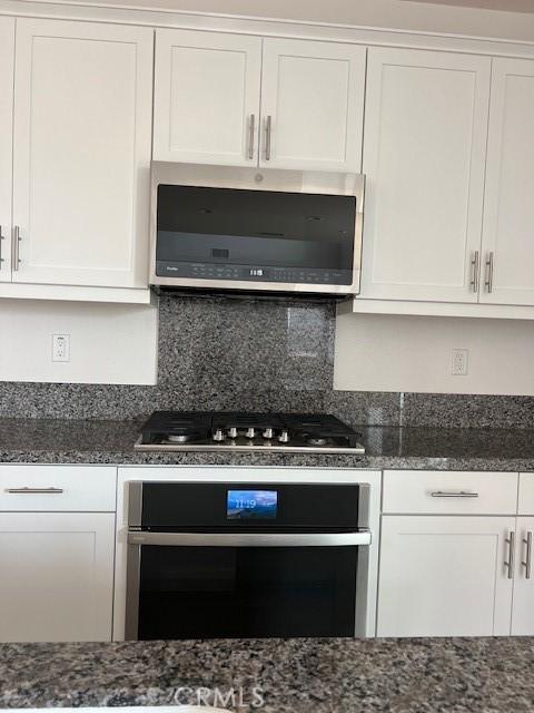 kitchen with white cabinets, appliances with stainless steel finishes, and dark stone countertops