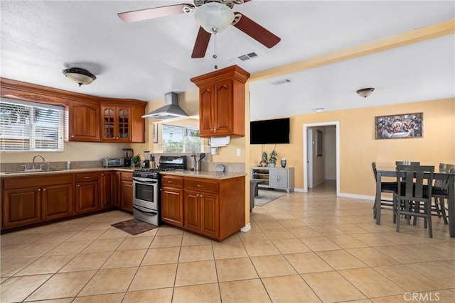 kitchen with light tile patterned floors, ceiling fan, gas range, wall chimney exhaust hood, and sink