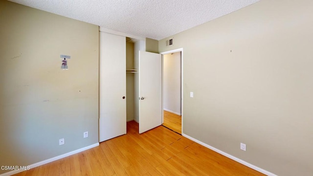 unfurnished bedroom featuring a textured ceiling, a closet, and light wood-type flooring