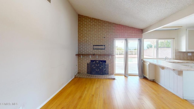 unfurnished living room with a textured ceiling, lofted ceiling, light hardwood / wood-style floors, sink, and a brick fireplace