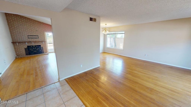 unfurnished living room featuring a brick fireplace, a textured ceiling, lofted ceiling, and light tile patterned flooring