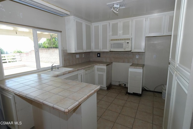 kitchen with kitchen peninsula, light tile patterned flooring, white appliances, tile counters, and white cabinets