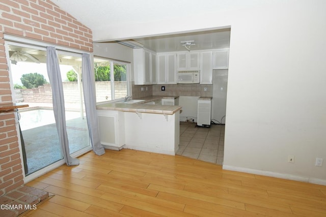 kitchen featuring white cabinets, decorative backsplash, sink, kitchen peninsula, and light wood-type flooring