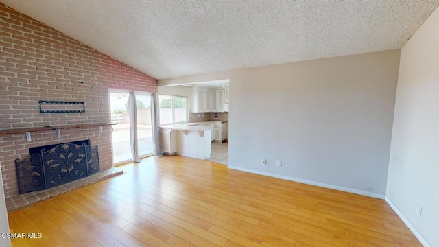 unfurnished living room featuring light wood-type flooring, lofted ceiling, a textured ceiling, and a fireplace