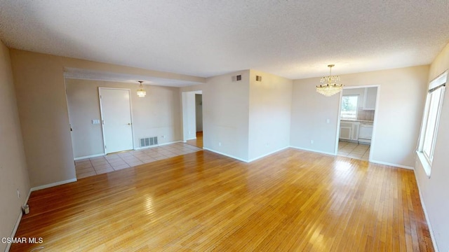 spare room with a notable chandelier, a textured ceiling, and light hardwood / wood-style floors