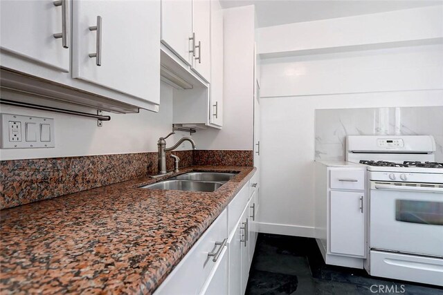 kitchen with dark stone countertops, white cabinets, white gas range oven, and sink