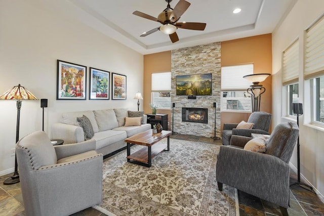 living room featuring ceiling fan, a raised ceiling, and a fireplace