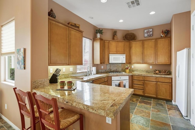 kitchen featuring sink, a kitchen bar, kitchen peninsula, and white appliances