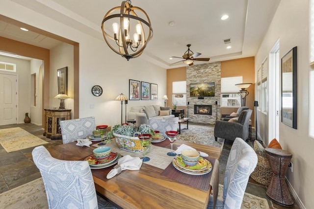 dining area featuring a fireplace, ceiling fan with notable chandelier, and a tray ceiling