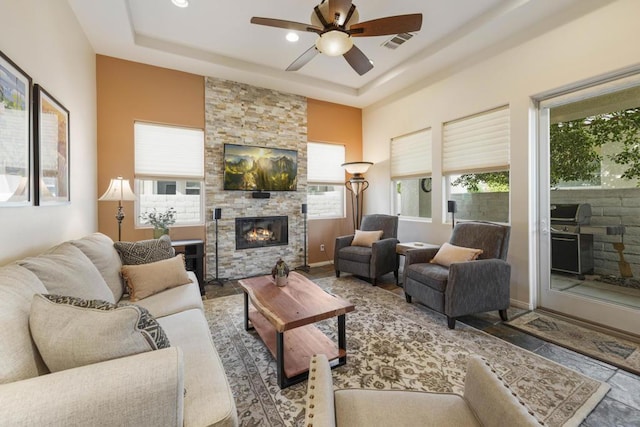 living room with ceiling fan, a fireplace, and a tray ceiling