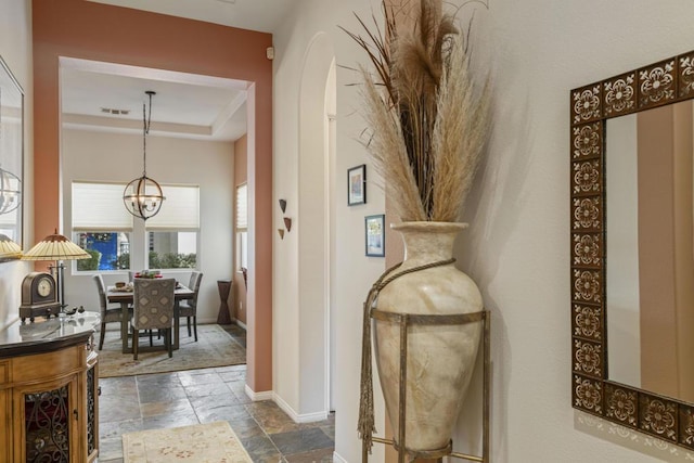 hallway with a raised ceiling and a chandelier