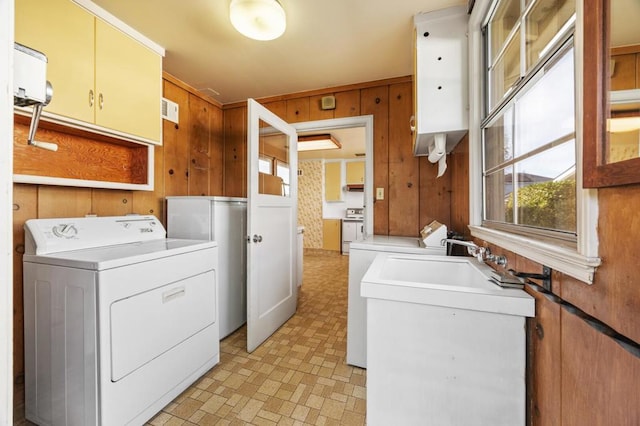 clothes washing area with wood walls, washer and dryer, and cabinets