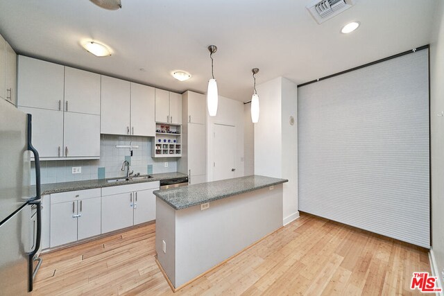 kitchen with backsplash, white cabinetry, hanging light fixtures, light wood-type flooring, and appliances with stainless steel finishes