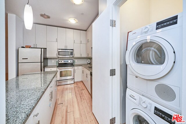 kitchen with stainless steel appliances, stacked washer / dryer, white cabinets, and hanging light fixtures