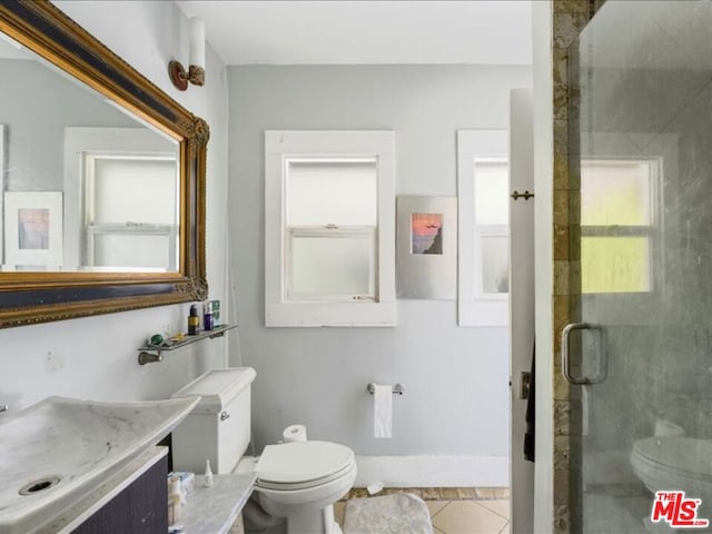 bathroom with a shower with door, vanity, tile patterned floors, and toilet