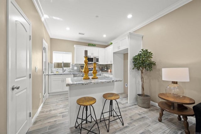 kitchen with light stone countertops, a kitchen island, white cabinetry, a breakfast bar, and stove