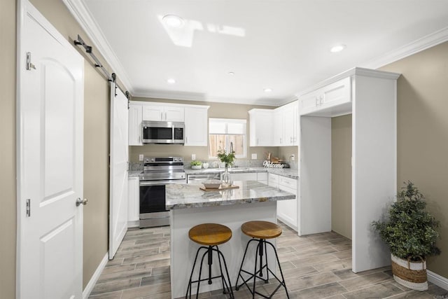 kitchen with a barn door, a kitchen island, white cabinetry, stainless steel appliances, and light stone counters