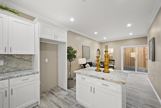 kitchen featuring light stone counters, backsplash, white cabinetry, and ornamental molding