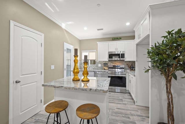 kitchen featuring tasteful backsplash, a kitchen island, light stone countertops, appliances with stainless steel finishes, and white cabinets