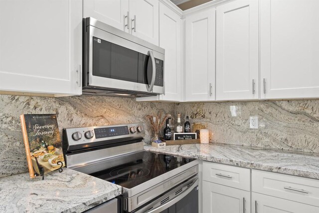 kitchen featuring stainless steel appliances, backsplash, white cabinetry, and light stone counters