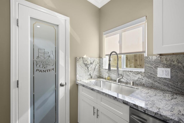 kitchen with backsplash, light stone countertops, stainless steel dishwasher, white cabinets, and sink