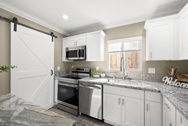 kitchen featuring white cabinets, stainless steel appliances, sink, ornamental molding, and a barn door