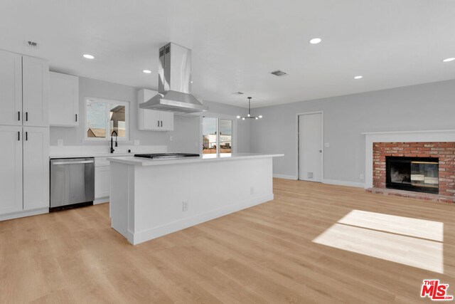 kitchen with exhaust hood, a fireplace, stainless steel dishwasher, white cabinetry, and hanging light fixtures