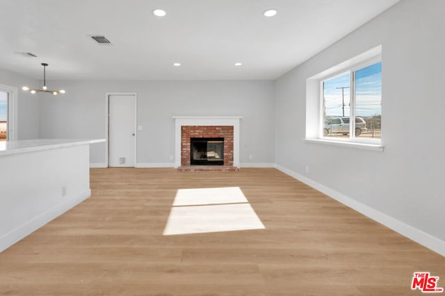 unfurnished living room with a brick fireplace, a chandelier, and light hardwood / wood-style floors