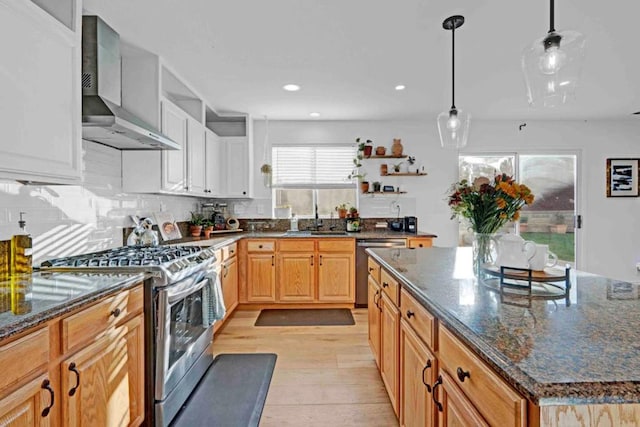 kitchen featuring decorative light fixtures, wall chimney exhaust hood, dark stone counters, and stainless steel appliances