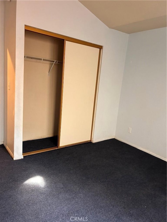 unfurnished bedroom with vaulted ceiling, a closet, and dark colored carpet