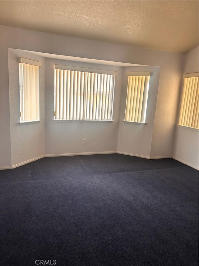 spare room featuring a textured ceiling and dark colored carpet