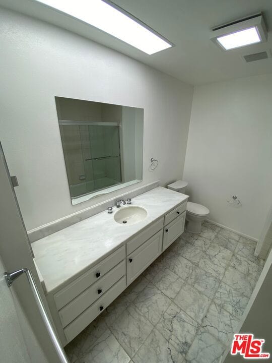 bathroom with toilet, vanity, and a shower with shower door