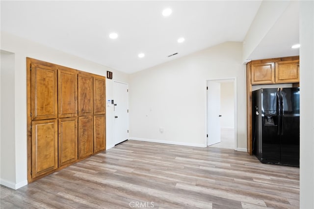 kitchen with lofted ceiling, light hardwood / wood-style flooring, and black fridge