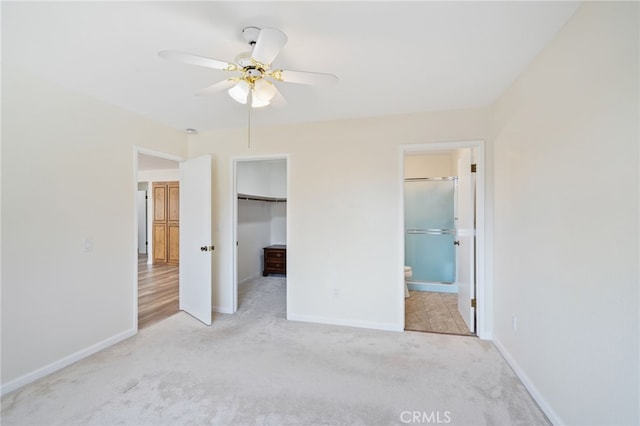 unfurnished bedroom with light carpet, a spacious closet, ceiling fan, ensuite bath, and a closet