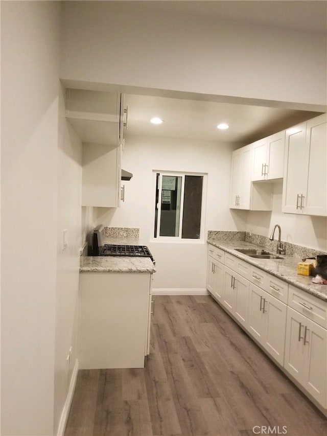 kitchen with wood finished floors, white cabinetry, a sink, light stone countertops, and range