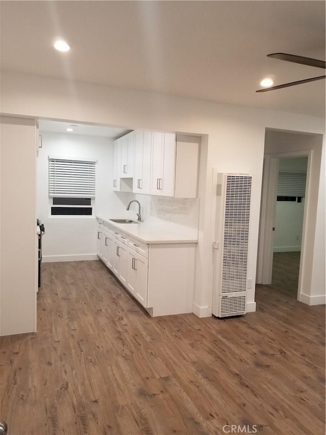 kitchen with a heating unit, white cabinets, dark wood-type flooring, light countertops, and a sink