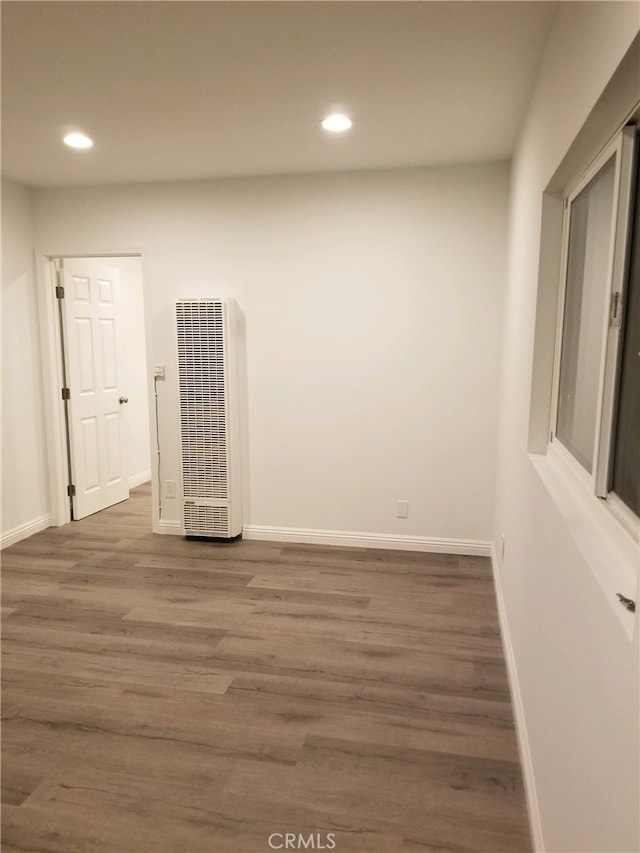 empty room with a heating unit, baseboards, wood finished floors, and recessed lighting