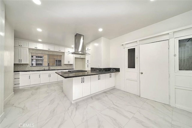 kitchen featuring marble finish floor, island exhaust hood, decorative backsplash, a sink, and a peninsula