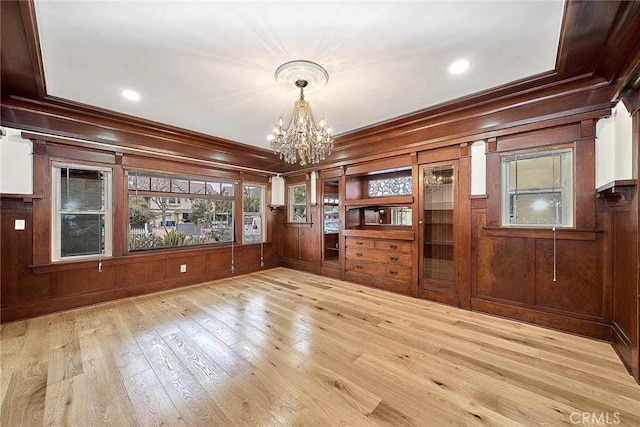 unfurnished dining area featuring crown molding, a notable chandelier, wood walls, and hardwood / wood-style flooring