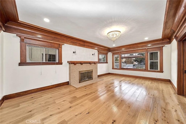 unfurnished living room featuring ornamental molding, light wood-type flooring, baseboards, and a tile fireplace